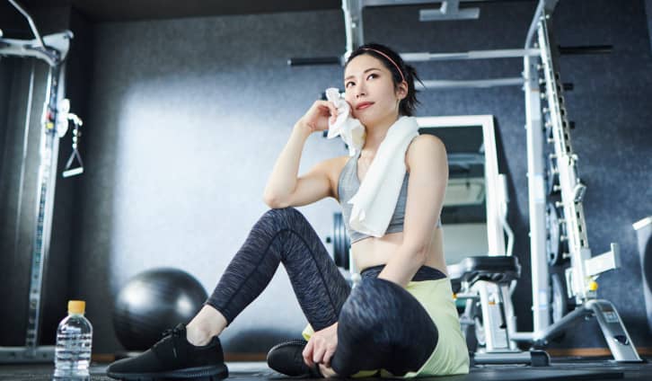 トレーニング後に汗を拭きながら休憩する女性。