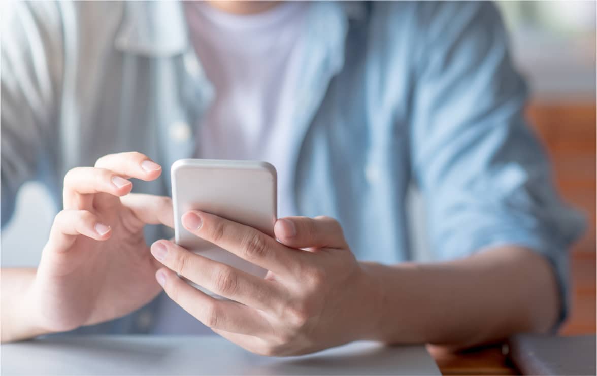 青いシャツを着た男性がスマートフォンを手にして画面を操作している。