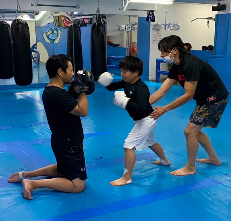 コーチと一緒に格闘技を学ぶ子どものトレーニング風景。