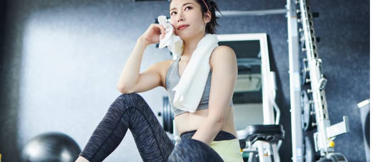 女性がTRXトレーニング中に体を持ち上げているシーン。トレーナーがサポート。
