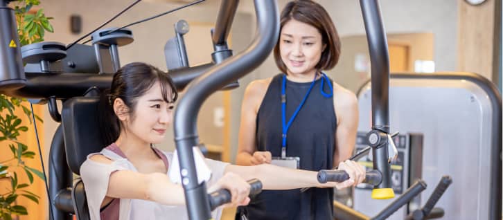水を入れたトレーニングバッグを使用して腹筋を行う女性と、それをサポートするトレーナー。