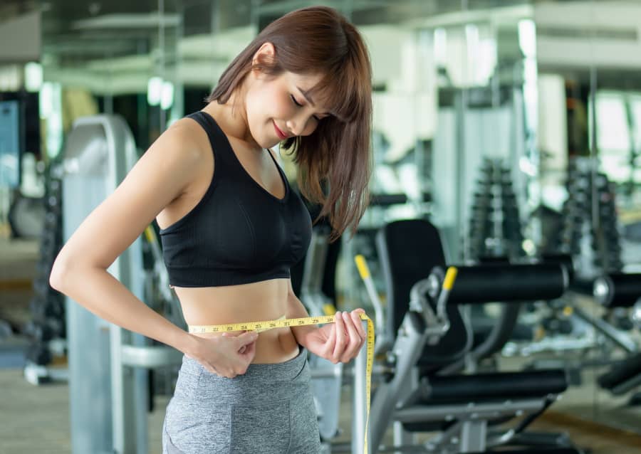 トレーニングの成果を確認するためにウエストを測る女性。
