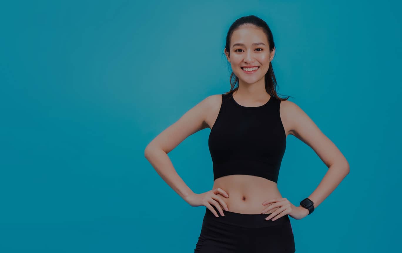 青い背景の前で笑顔を見せるフィットネスウェアの女性。